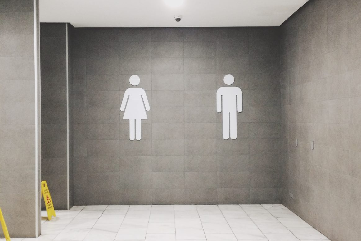 Empty bathroom, large white tiles on floor and large gray tiles on walls. Large male and female bathroom symbol figures on wall