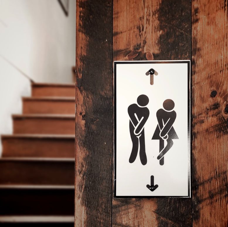 Wooden steps leading to hallway, bathroom sign in right of image with male and female bathroom figures crossing their legs