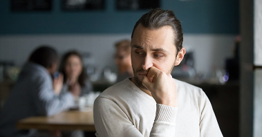 A man sits alone, feeling isolated, while others socialize around him.