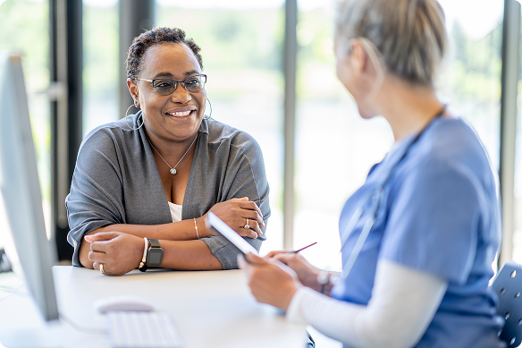 A smiling woman discusses clinical trials with a nurse holding a clipboard.