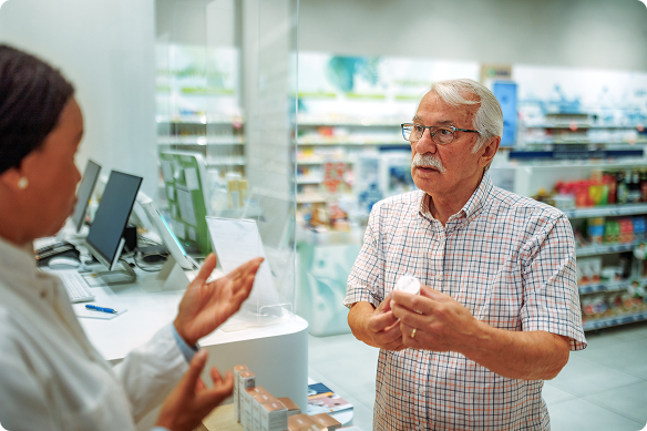 Man holding pill bottle discussing medication with female pharmacist