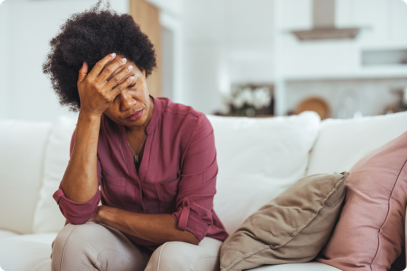 An exhausted woman sits on her couch, holding her head