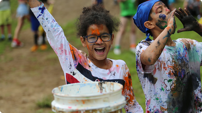 Video being developed, but if not ready, use image  A girl and boy, covered in paint, having a grand time in color wars at Camp Oasis.