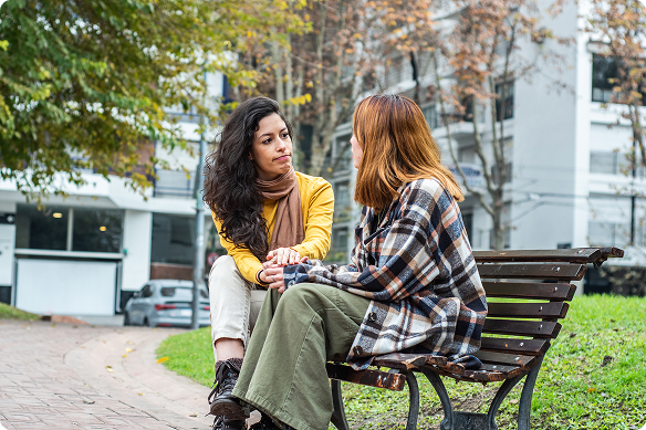 Two women talk in a park, one comforting the other while listening to her.