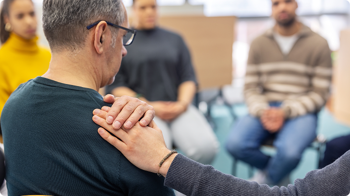 Hand is placed on older man’s shoulder at support group.