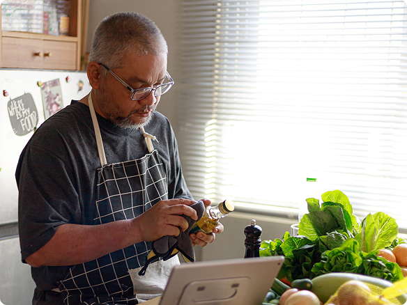 An adult man cooks vegetables in his kitchen while reading a recipe on his tablet.