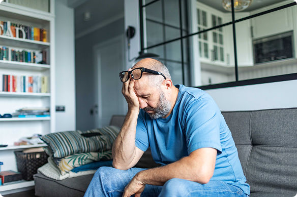 Exhausted man holds his head as he sits on his couch.