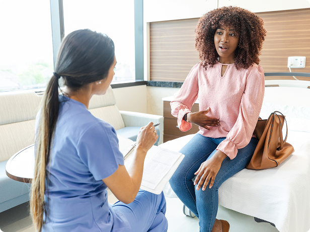  A woman sits on an examining table while gesturing at her abdomen and conversing with her doctor.