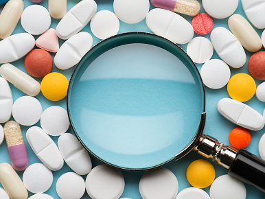 A magnifying glass surrounded by different colored pills.