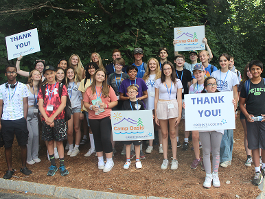 A large group of campers holding up Camp Oasis and Thank You signs.
