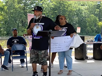 A man on stage giving a speech while a woman holds an oversized check behind him. 