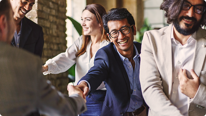 Diverse business team smiling and greeting with a handshake in a bright office, conveying warmth, collaboration, and a welcoming atmosphere.