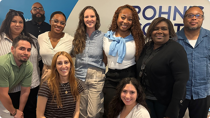 Group of ten coworkers from the Diversity, Equity and Inclusion Employee Resource Group smiling together in an office, posed in two rows before a blue-and-white “Crohn's & Colitis Foundation" logo.