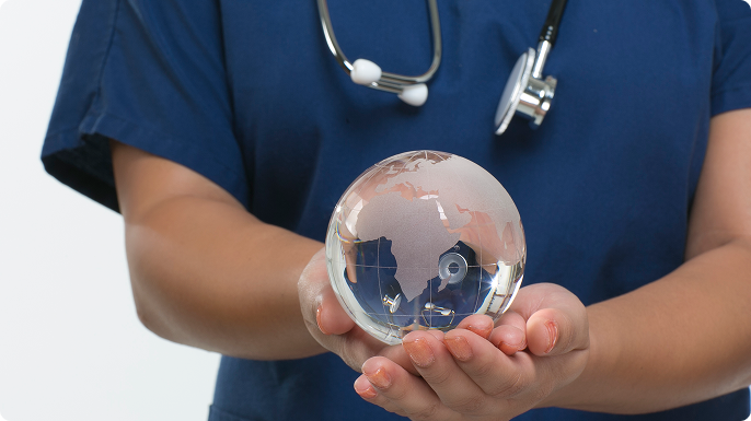 Healthcare professional in blue scrubs holds a transparent globe, with a stethoscope around their neck, symbolizing global healthcare and care.