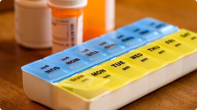A weekly pill container sitting on a table with other pill bottles