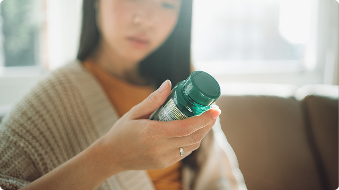 A young woman is holding and examining the label on a bottle of supplements
