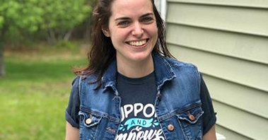Young woman, outdoors, in denim vest smiling to the camera