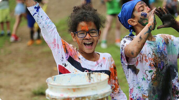 A girl and boy, covered in paint, having a grand time in color wars at Camp Oasis