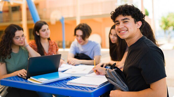 A male teen turns and smiles as he is studying with his friends