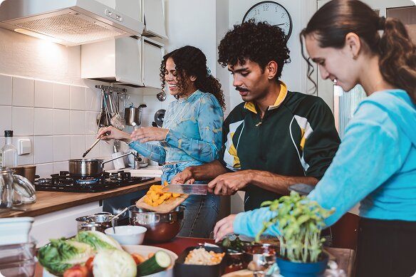 Two young women and a man prepare food in an apartment kitchen