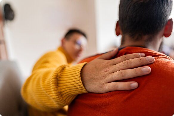A man places a supportive arm on the shoulder of his friend