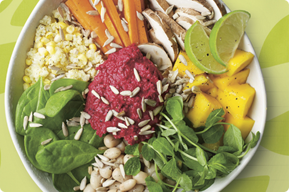 Colorful healthy Buddha bowl with beet hummus, spinach, carrots, mushrooms, mango, lime, beans, greens, and sunflower seeds.