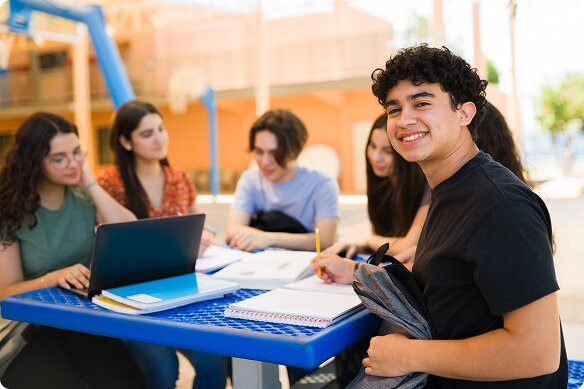 A male teen turns and smiles as he is studying with his friends