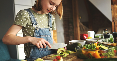 A young girl cuts vegetables while preparing a meal