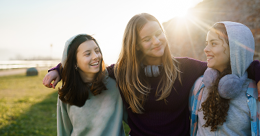 Three teen girls hug each other supportively while out in the sunshine