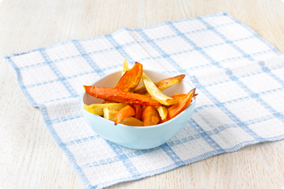 Blue bowl of crispy orange and golden vegetable chips sits on a blue-and-white checked cloth atop a light wood table, creating a cozy snack scene.