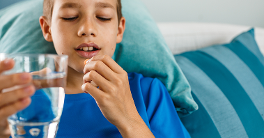 A young boy prepares to take his medication as he holds a glass of water in one hand, and a pill in his other hand