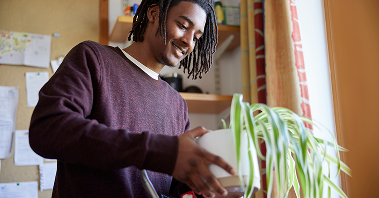A young man unpacks a plant in his college dorm room