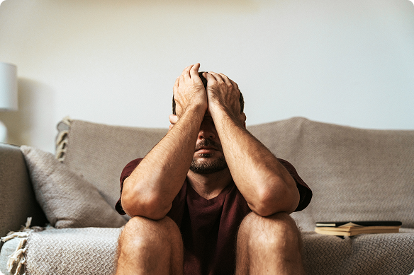 A man sits on the floor, elbows on knees, hands hiding his face