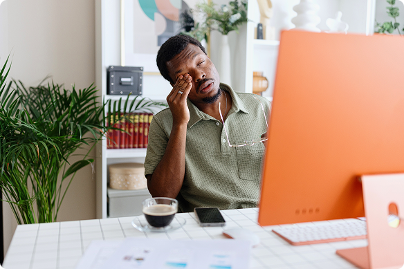 A man rubs his eyes while sitting in front of his computer in his office
