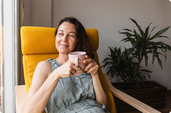 A woman sips tea, content, as she looks out her window while sitting in a comfy chair