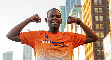 Young man in Team Challenge athletic jersey flexes arms, smiling towards camera