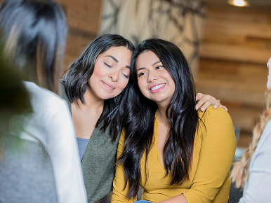 A young woman hugs another young woman in support