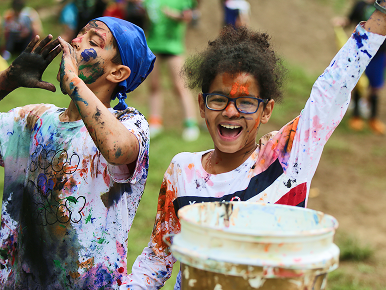 A girl and boy are covered in paint and looking triumphant during color wars at Camp Oasis