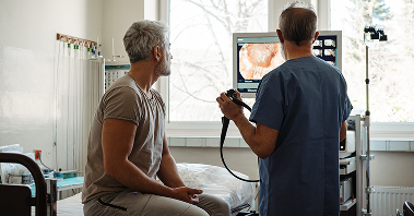 Male patient views results of his colonoscopy on screen while discussing with his doctor.