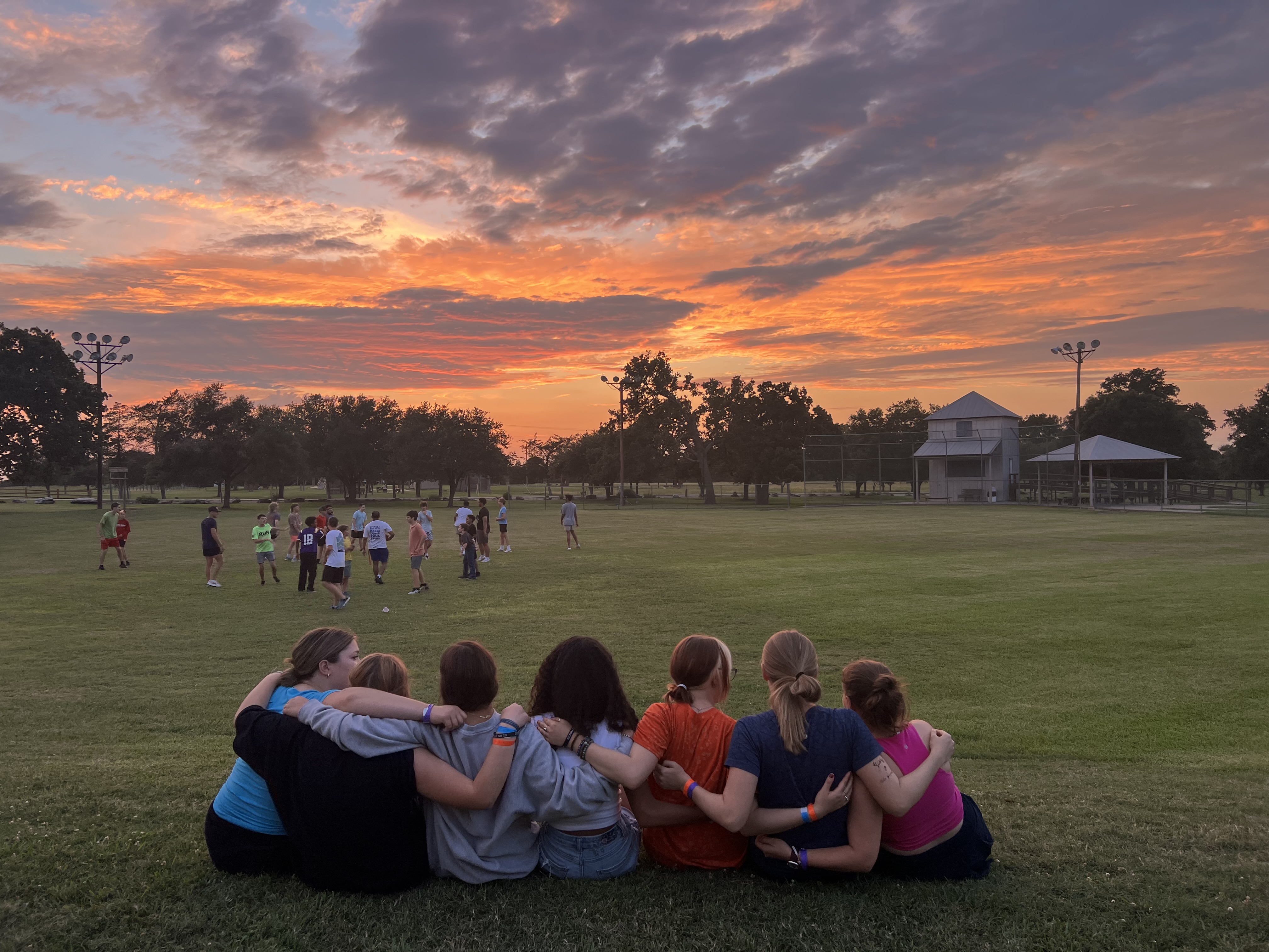 Campers sit side by side with arms around one another looking into the sunset