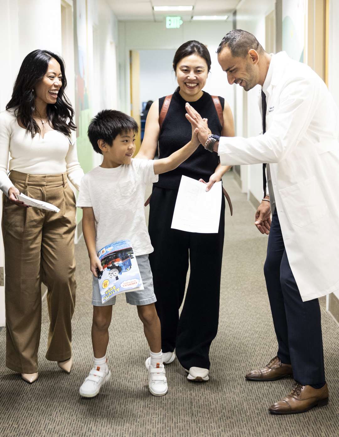 Image of a smiling doctor giving a child a high-five. The child, a boy in elementary school, stands between two women.