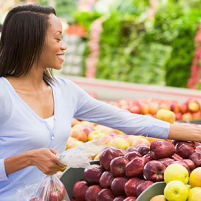 Woman shopping for fresh produce in a grocery store, selecting apples for a healthy IBD-friendly diet