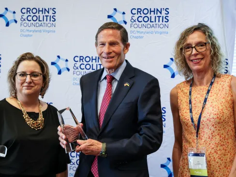 3 people standing in front of Crohn's and Colitis Foundation banner