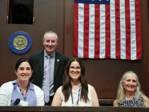 4 people at a courtroom-like setting in front of the US flag