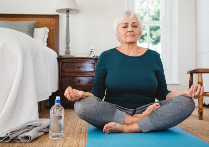 Senior woman meditating on yoga mat indoors