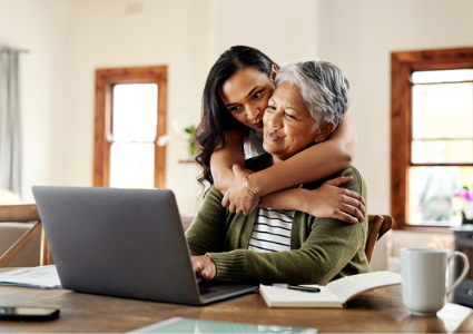 Daughter hugging senior mother; working on laptop together