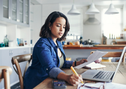 Woman working at laptop and writing down notes