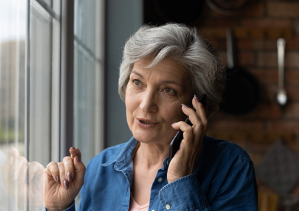 Older Latinx woman making phone call by window