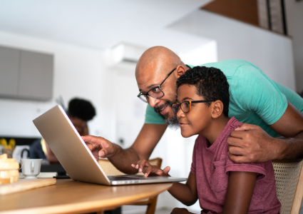 Latinx father helping teen son at computer
