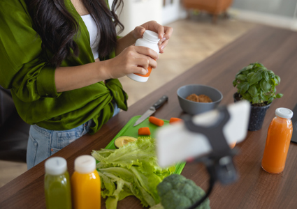Woman opening bottle of vitamins at counter with vegetables and juice nearby